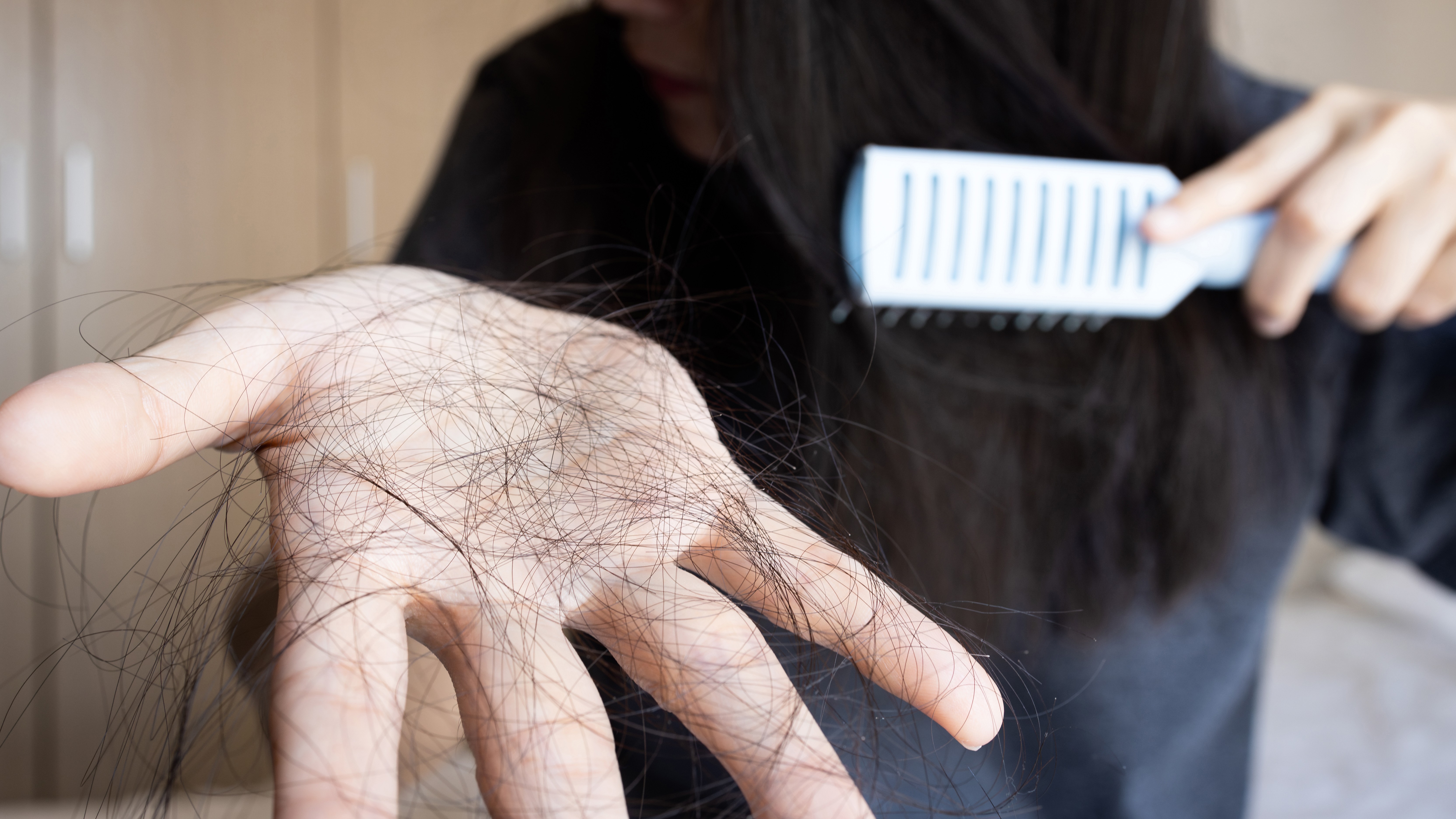 a woman holds a clump of hair in one hand while brushing her remaining hair with the other