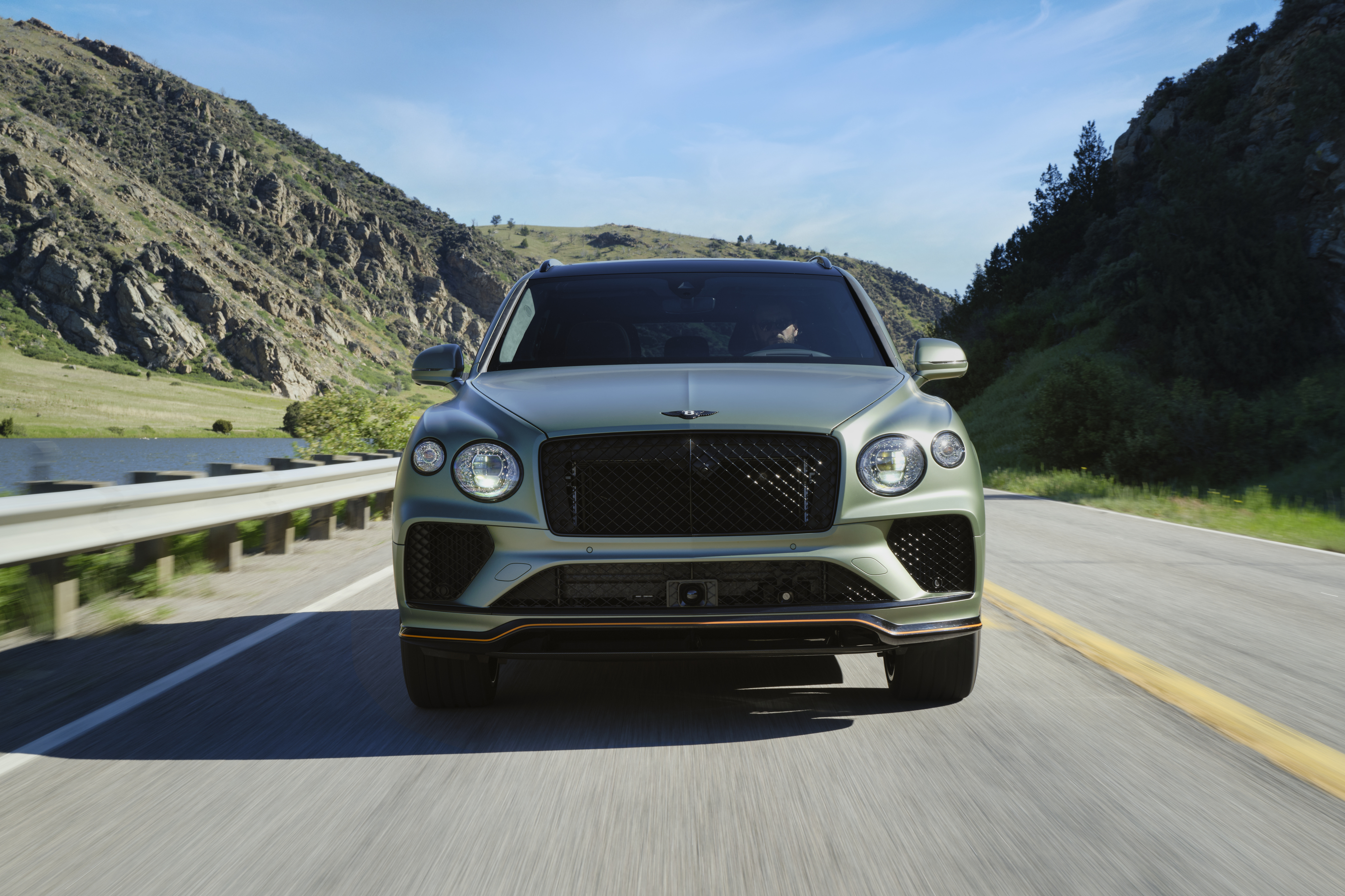 A front view of the Bentley Bentayga Speed, driving down a road surrounded by mountains