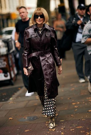 foto gaya jalanan Anna Wintour mengenakan mantel kulit cokelat di atas gaun bermotif dengan sepatu bot ke peragaan busana JW Anderson musim semi 2025