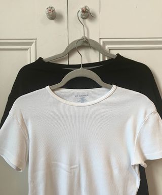 A black tshirt and a white tshirt hanging on grey hangers connected with a soda can ring pull