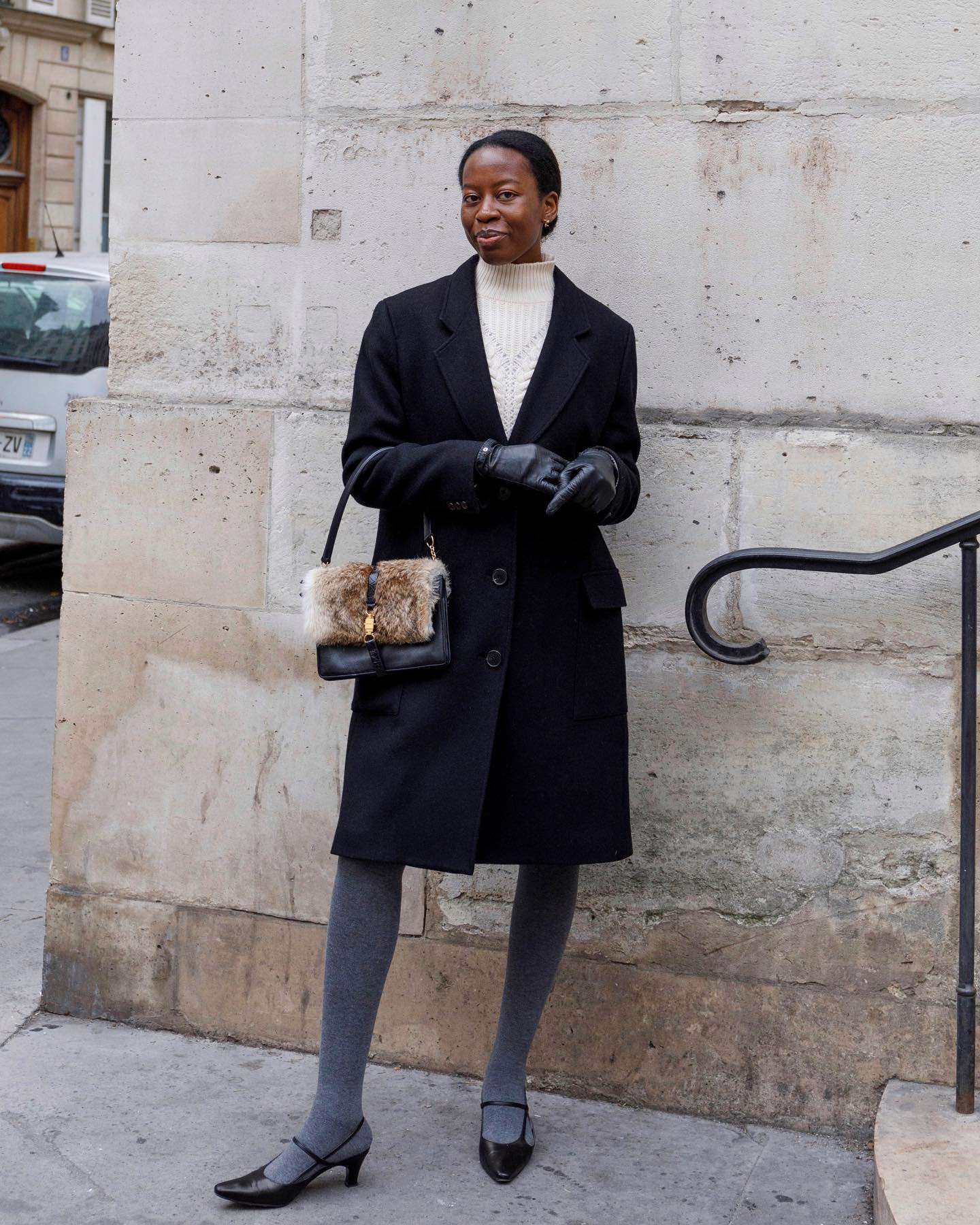 @sylviemus_ wears a white roll neck with a black coat, leather glove, grey tights and black shoes.