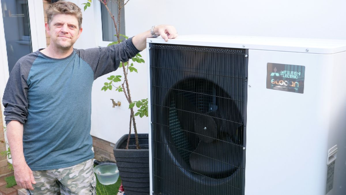 man stood next to air source heat pump outside house