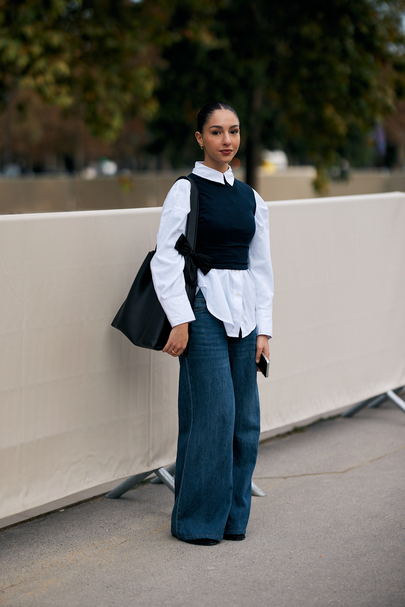 woman wearing button-down shirt, sweater vest, jeans, and a tote bag