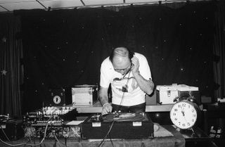 A black & white photo of an older man DJ-ing.