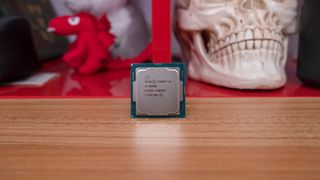 En Intel Core i5-12600K står upplutad på ett träfärgat bord med en röd figur och en dekorativ döskalle i bakgrunden.