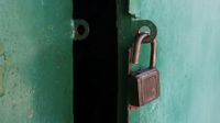 A close up of a green metal door fitted with an unlocked padlock