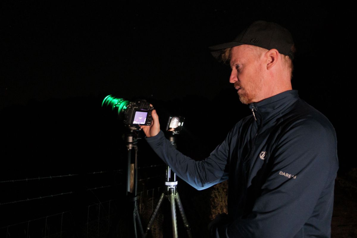 Pixel phone and Nikon mirrorless camera side by side mounted to tripods at night, with the astrophotography mode active on the Pixel and Tim Coleman controlling the camera