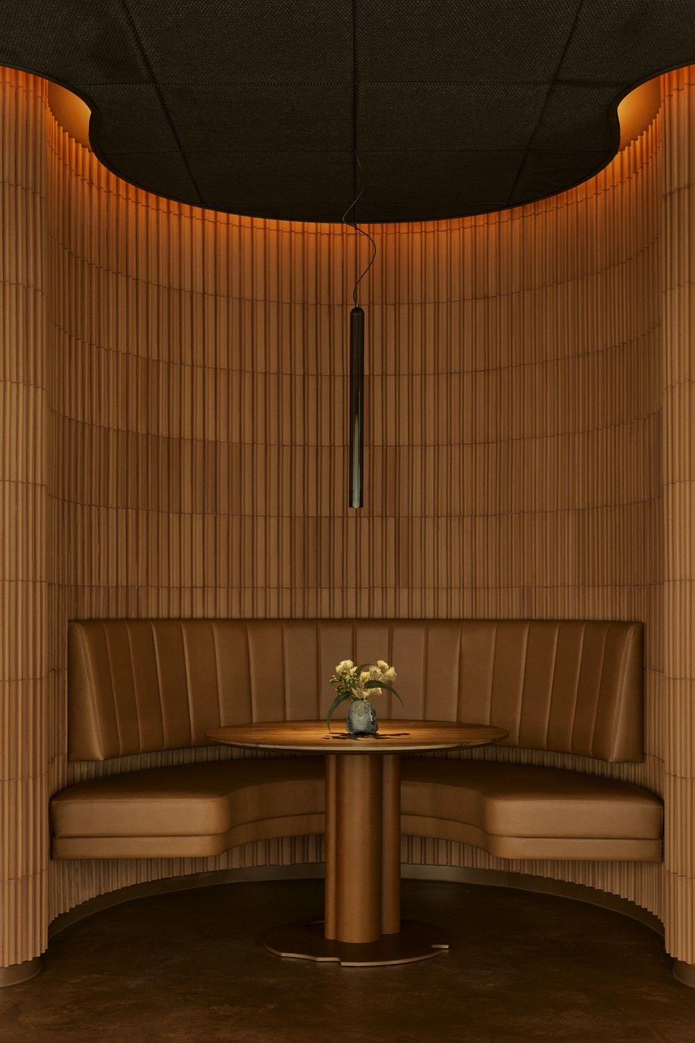 An all-terracotta restaurant booth decorated with a brick-clad arched booth inside of which you find brown leather banquettes with matching backs, and a round table in wood topped by a flower vase.