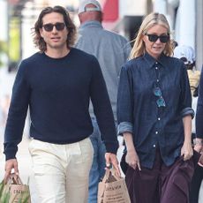 Gwyneth Paltrow walks down the street wearing burgundy trousers with burgundy flats and a denim shirt.
