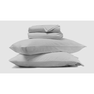 A pile of bedding. Two pillows on the bottom with two folded sheets stacked on top in a stone grey color