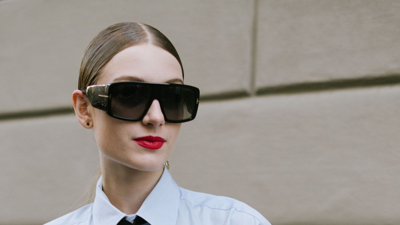 a woman with a bright red lip wearing sunglasses and a slicked back bun - best by terry products