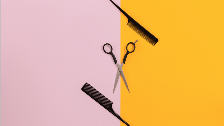 Hairdressing scissors and comb on pink and yellow background
