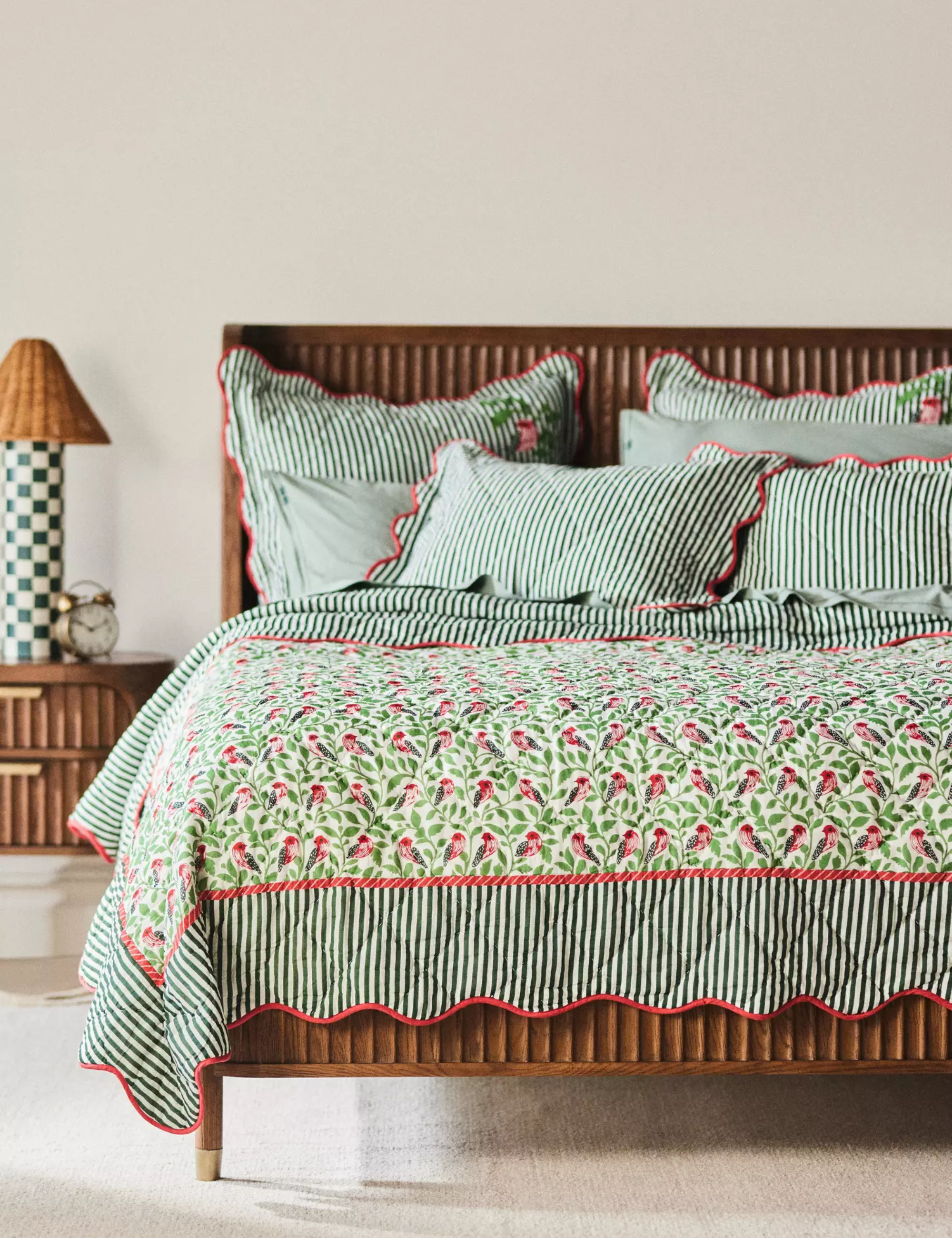 Floral block-printed quilt with scalloped borders styled on a wooden bed frame featuring a fluted texture, set inside a sunny, neutral bedroom
