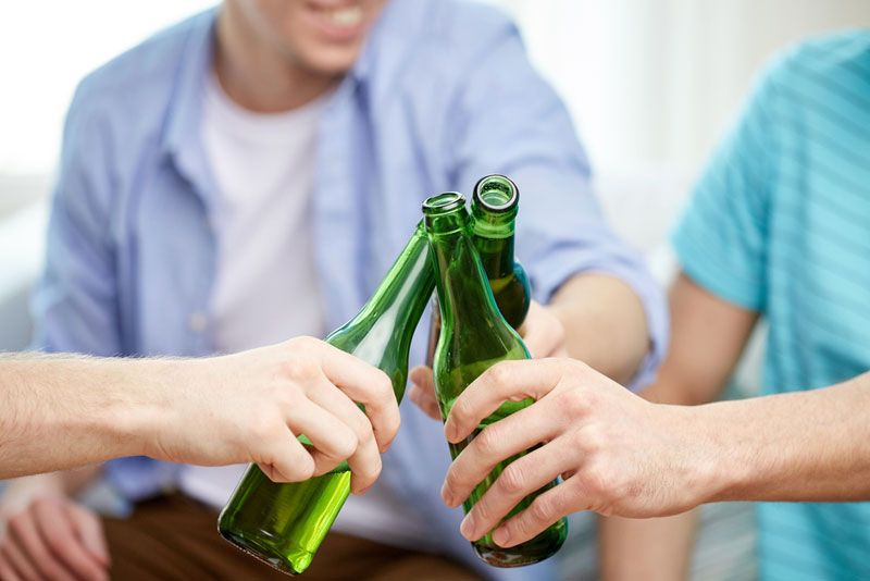 People clinking beer bottles at home.