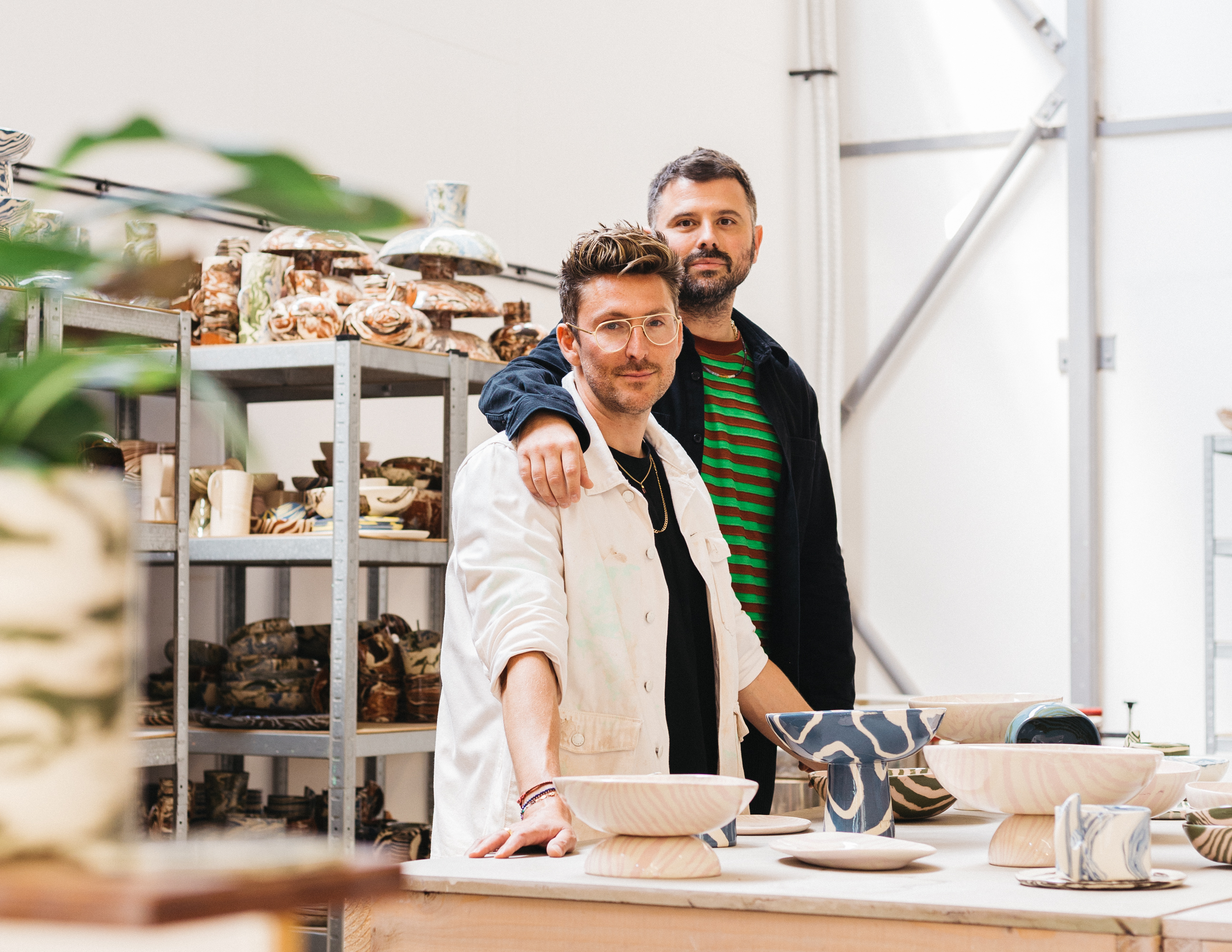 Two men, one with his arm around the other's shoulders, in a ceramics studio