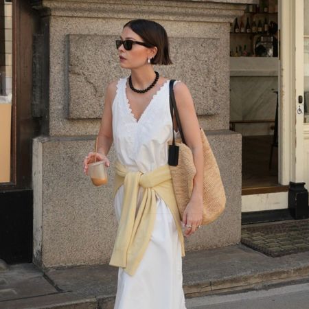 Woman wears white embroidered dress, yellow cardigan and woven raffia bag