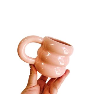 A hand holding a small pink ribbed mug