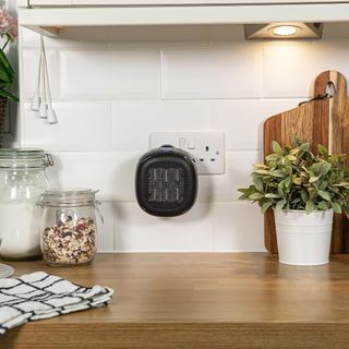 Russell Hobbs 700W Ceramic Plug In Heater plugged into a kitchen wall socket above a wooden countertop
