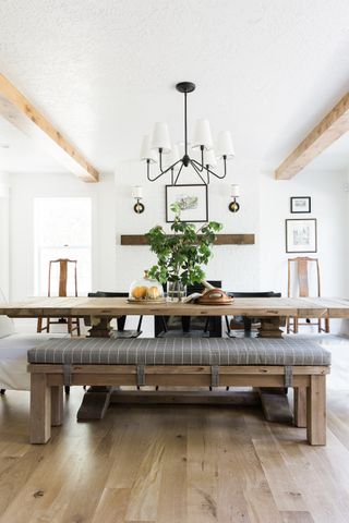 rustic dining room with white walls, wooden table and bench with black pendant with white shades, white flooring