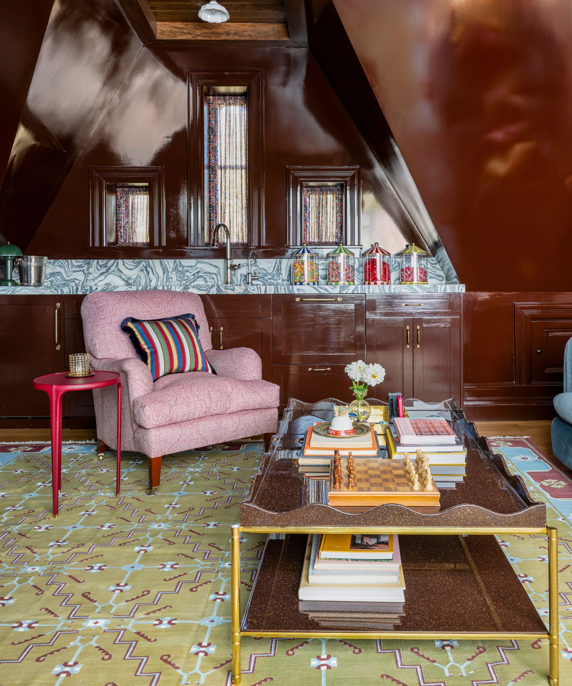 a top floor lounge in a brownstone home with glossy brown walls and cabinetry, a small kitchenette, and a layered lounge area
