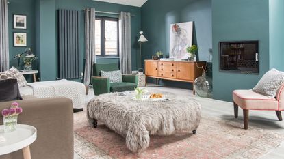Teal painted living room with oversized footstool covered in faux fur throw and a vintage sideboard