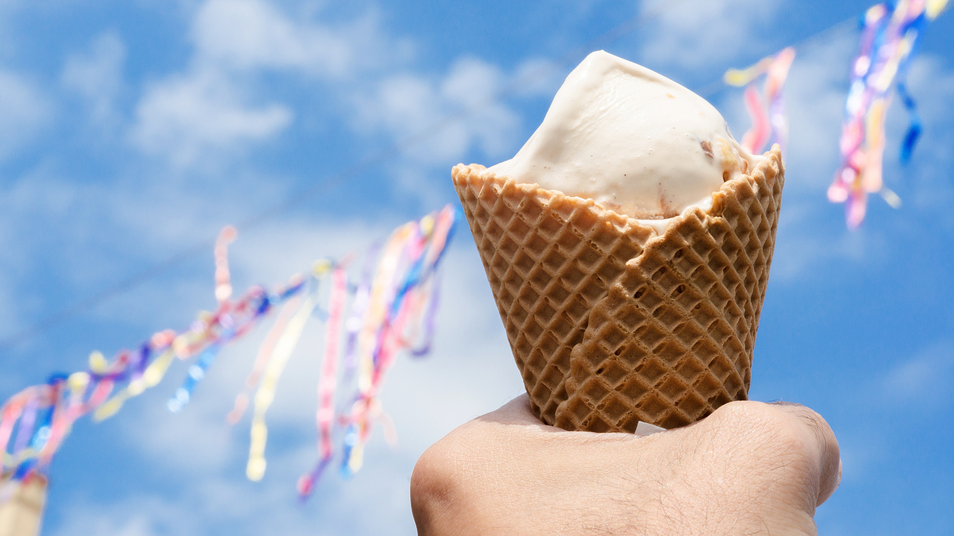 A hand holds up an ice cream cone. Streamers in the background.