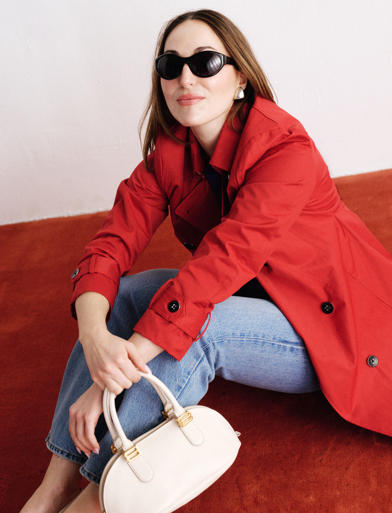 Anna wears a red trench coat, jeans, and a white bag.