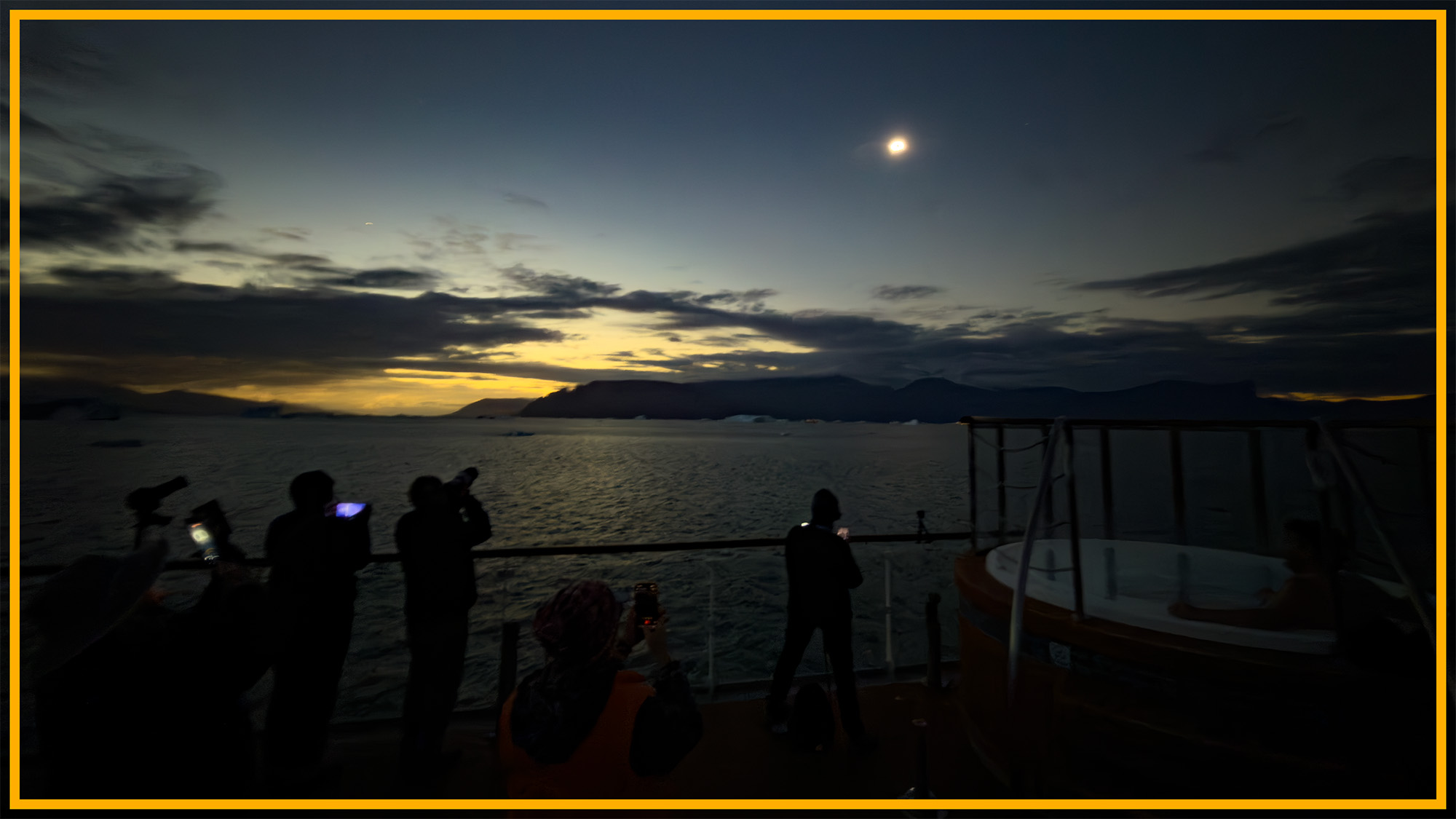 A view of people standing on a beach looking up at a dim sun with a yellow border around the image.