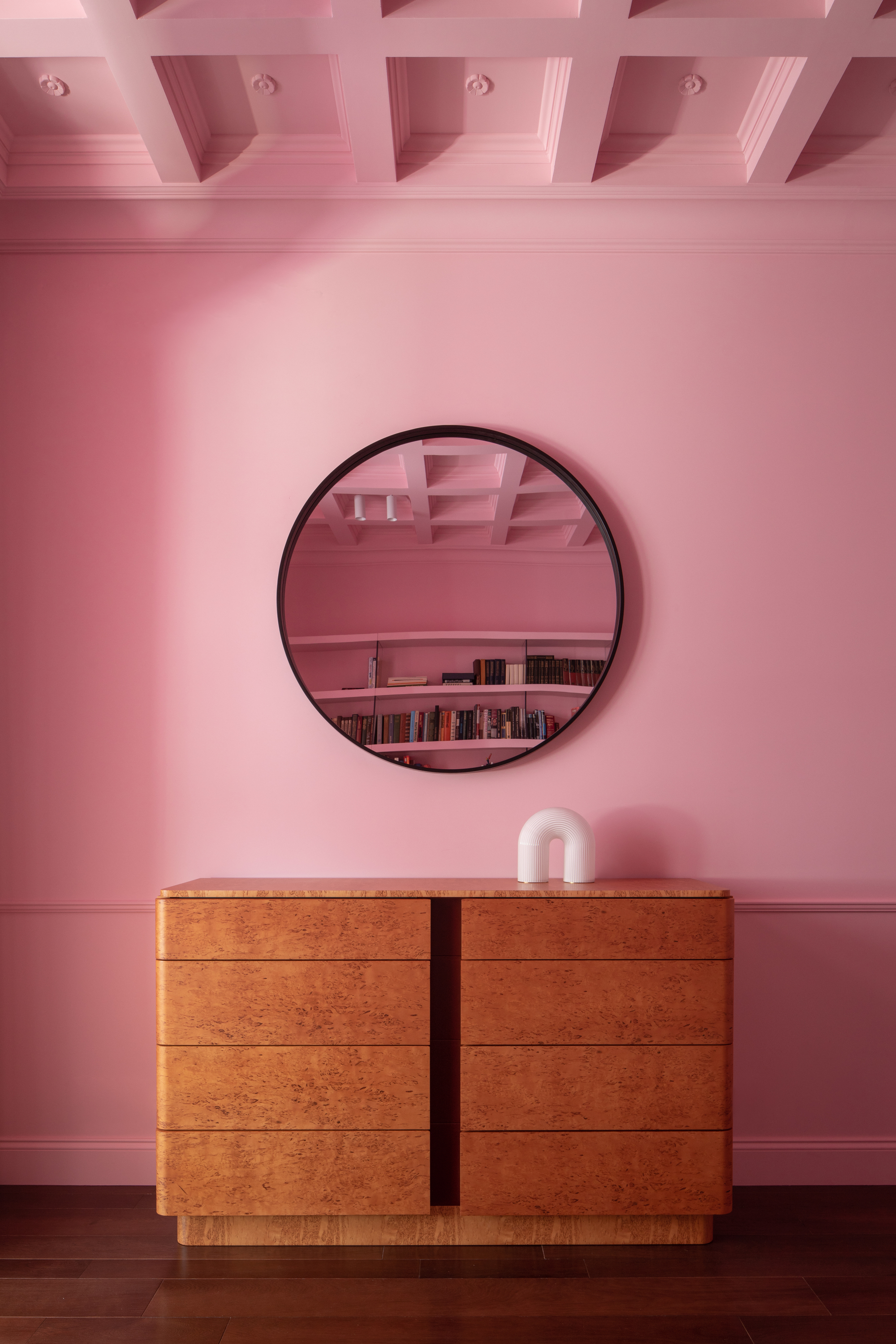 Image of a bubblegum pink entryway with a burl wood console and a round mirror hanging over it.