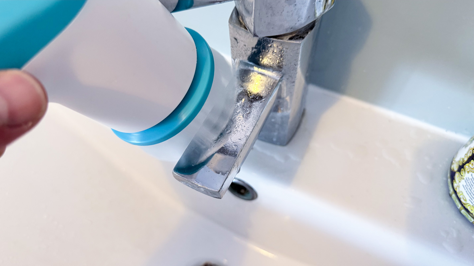 The Scrub Buddi in hand being used to clean a faucet