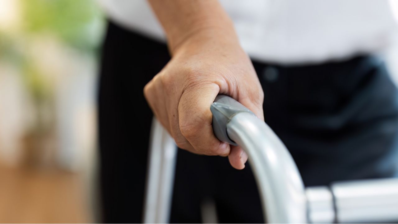 A man uses a walker, only his hand and torso showing.