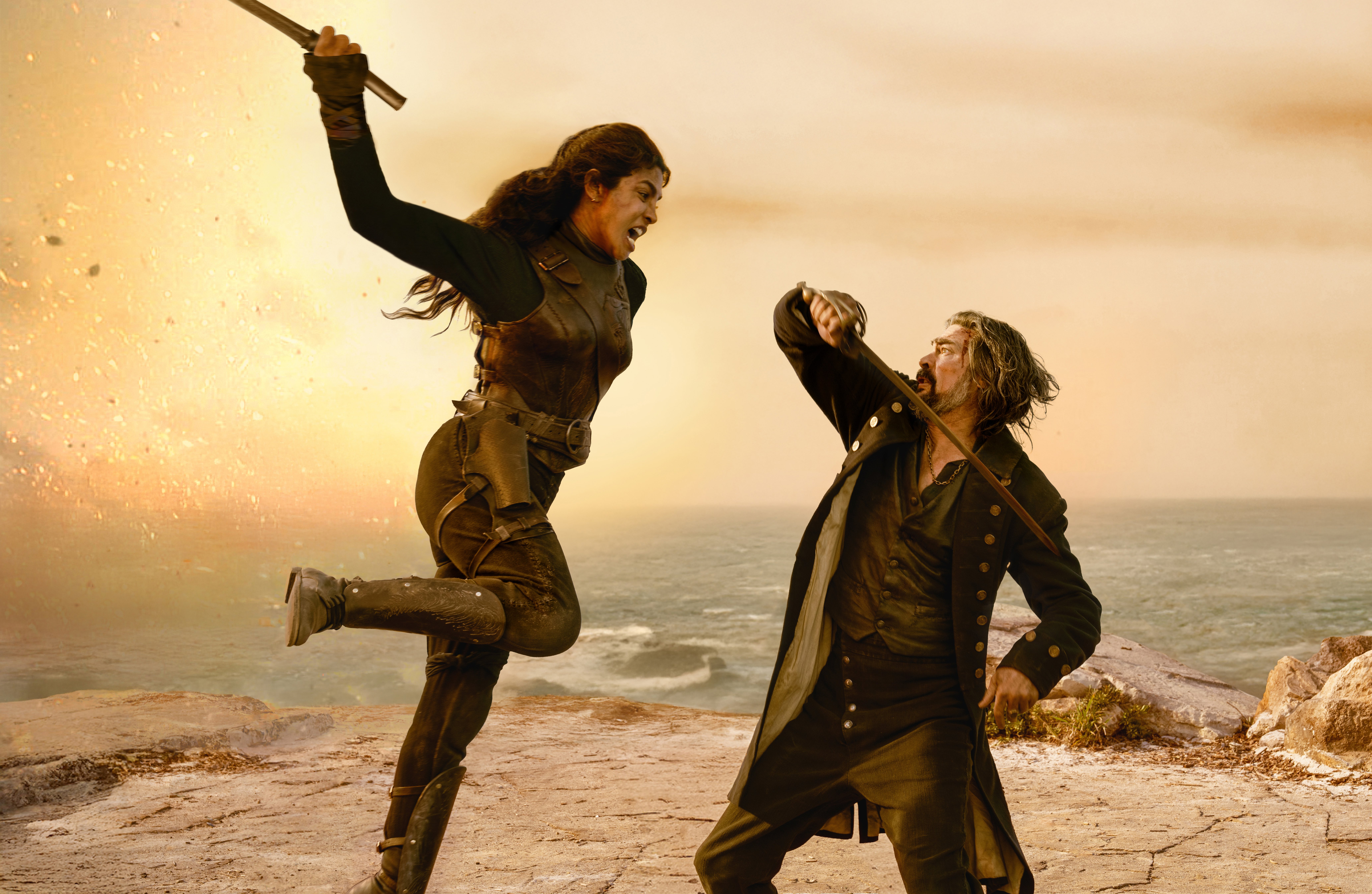 Priyanka Chopra Jonas as pirate ercell jumping up to fight karl urban as Captain Connor on a seaside cliff against a fire in the distance in a still from the movie the bluff
