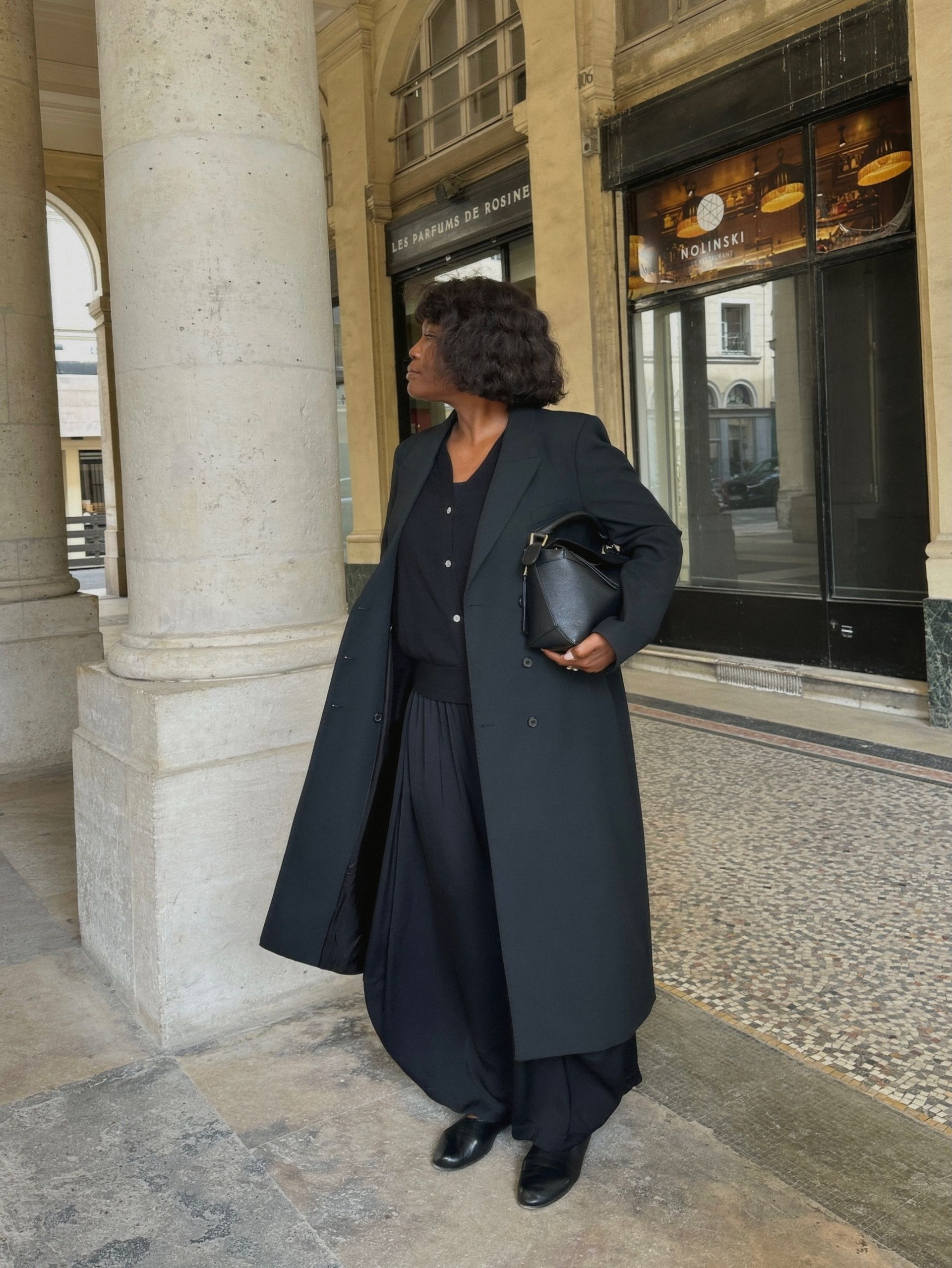 An image of an influencer in Paris wearing a tailored winter coat with balloon trousers and high-vamp flats holding a black leather handbag