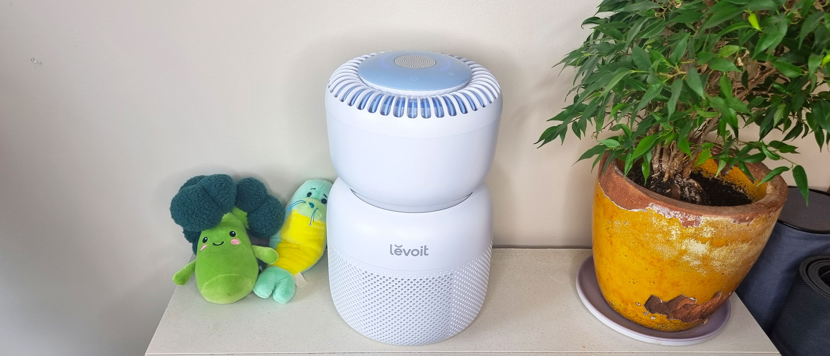 Levoit Sprout air purifier sat next to two plushie toys and a houseplant