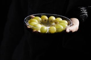 A person holds a bowl of 12 green grapes