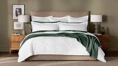 The world&#039;s best duvet insert, the Boll &amp; Branch Down Duvet Insert, on a bed with white pillows and green blankets against a green wall.