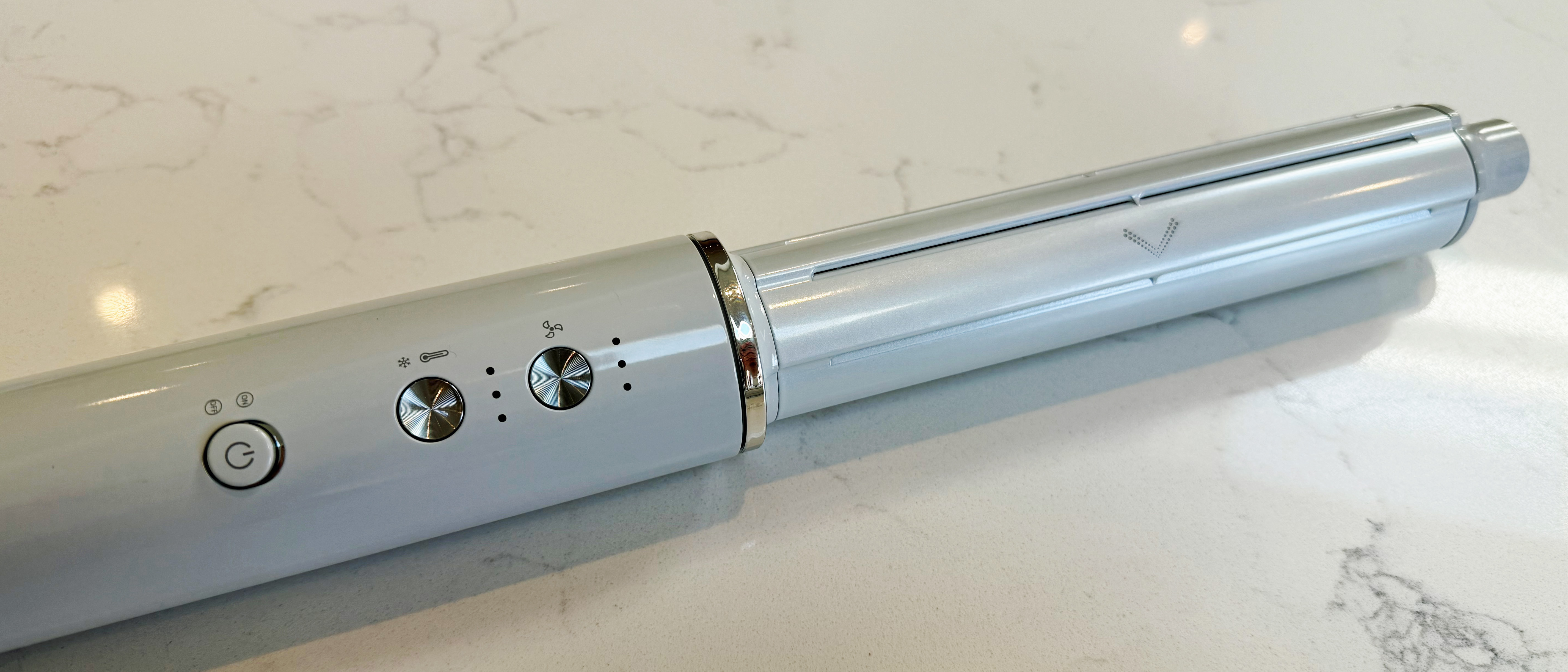 Close-up of the T3 Aire 360 base lying on a marble surface, showing the power button, temperature dial and speed dial controls on the lower body, with a curling barrel attachment connected at the top