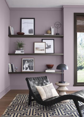 Corner view of a purple and black living room. There are black floating shelves with picture frames on them and a wavy black lounge chair on top of a black and white patterned rug