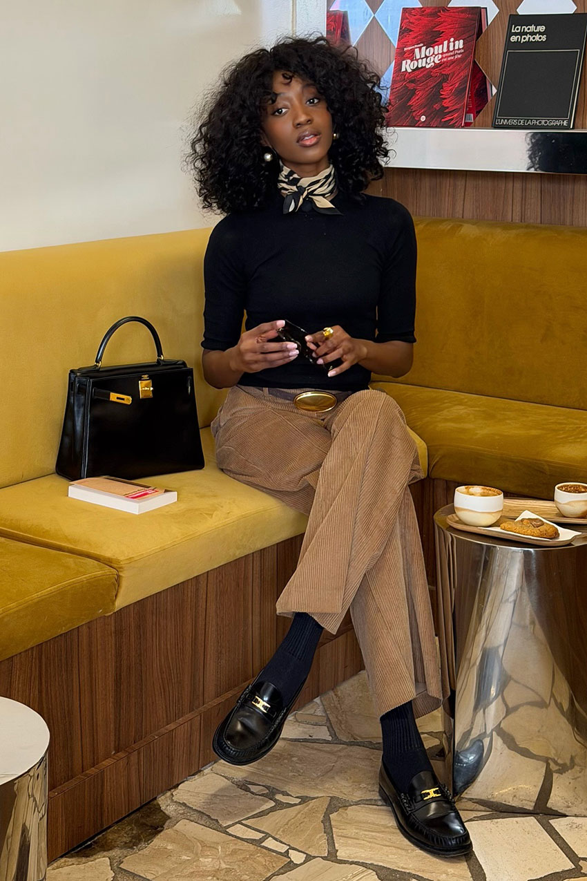 a woman wearing a black sweater, brown pants, and black loafers
