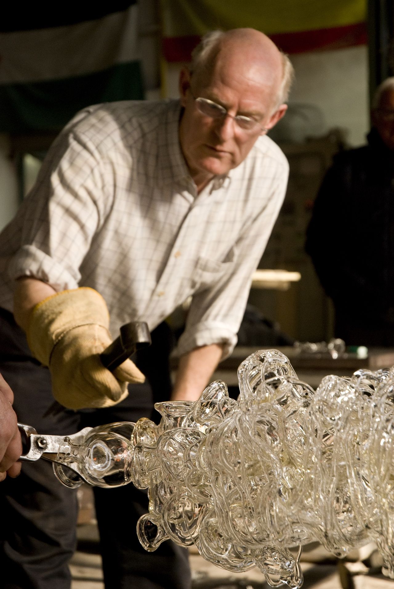 A man at work in a glass furnace perfects the structure of his transparent glass chandelier.