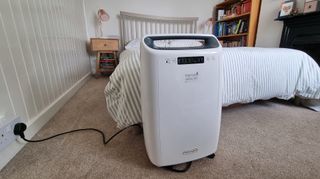 De'Longhi AriaDry dehumidifier in front of bed with green striped duvet