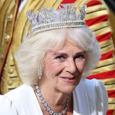 Queen Camilla wears a white dress, a diamond necklace, and a glittering diamond tiara