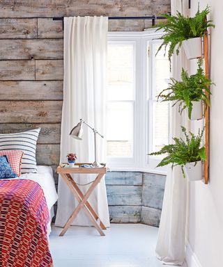 Bedroom ideas for teenagers with rustic gray-washed wood panels, house plants and red patterned bed throw.