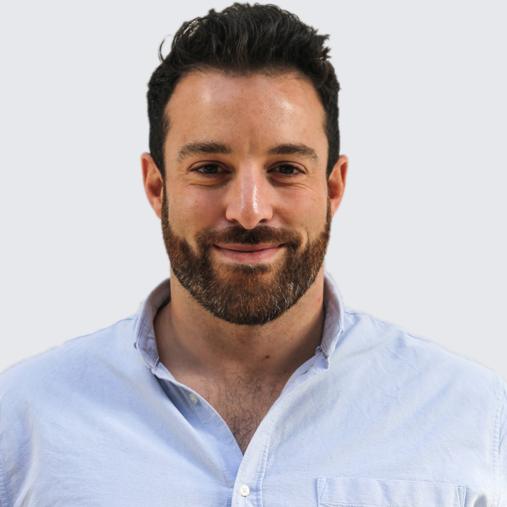 man with short dark hair, trimmed beard and moustache wearing blue shirt smiling at camera