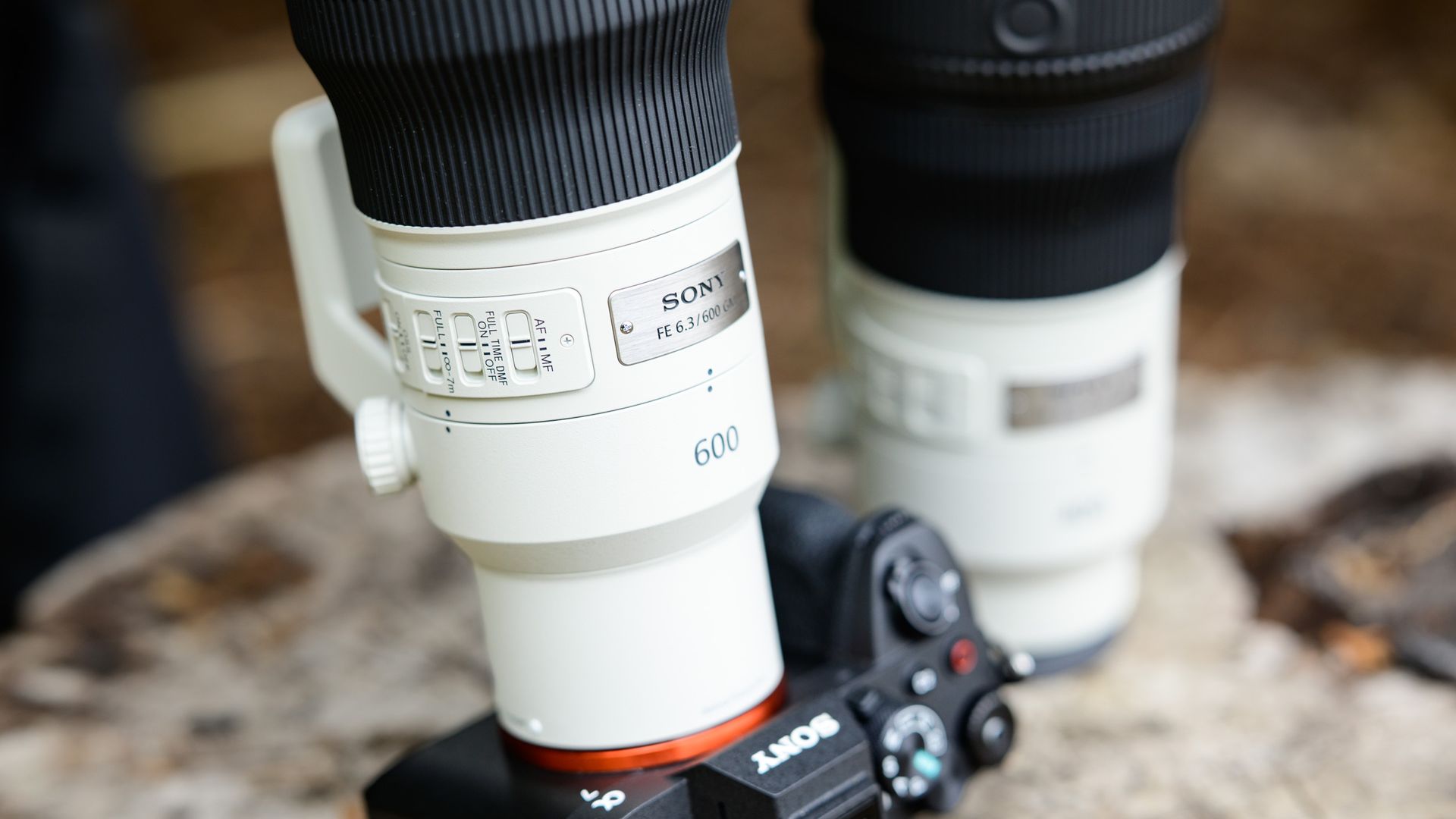 Sony FE 400mm F4.5 GM OSS and Sony FE 600mm F6.3 GM OSS super-telephoto lenses on a tree stump, with the 600mm attached to a Sony A7R V camera, closeup of the lens controls
