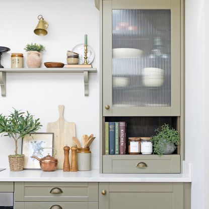 Kitchen with light green painted kitchen cabinetry and open shelving, decorated with cookbooks, crockery, and spices