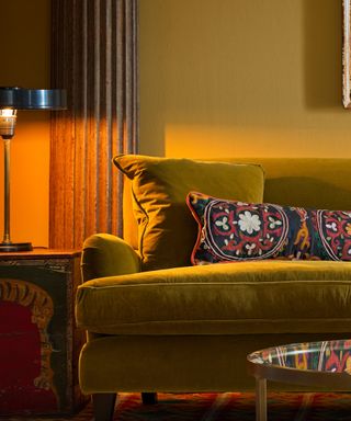 A green velvet sofa with an embroidered pillow