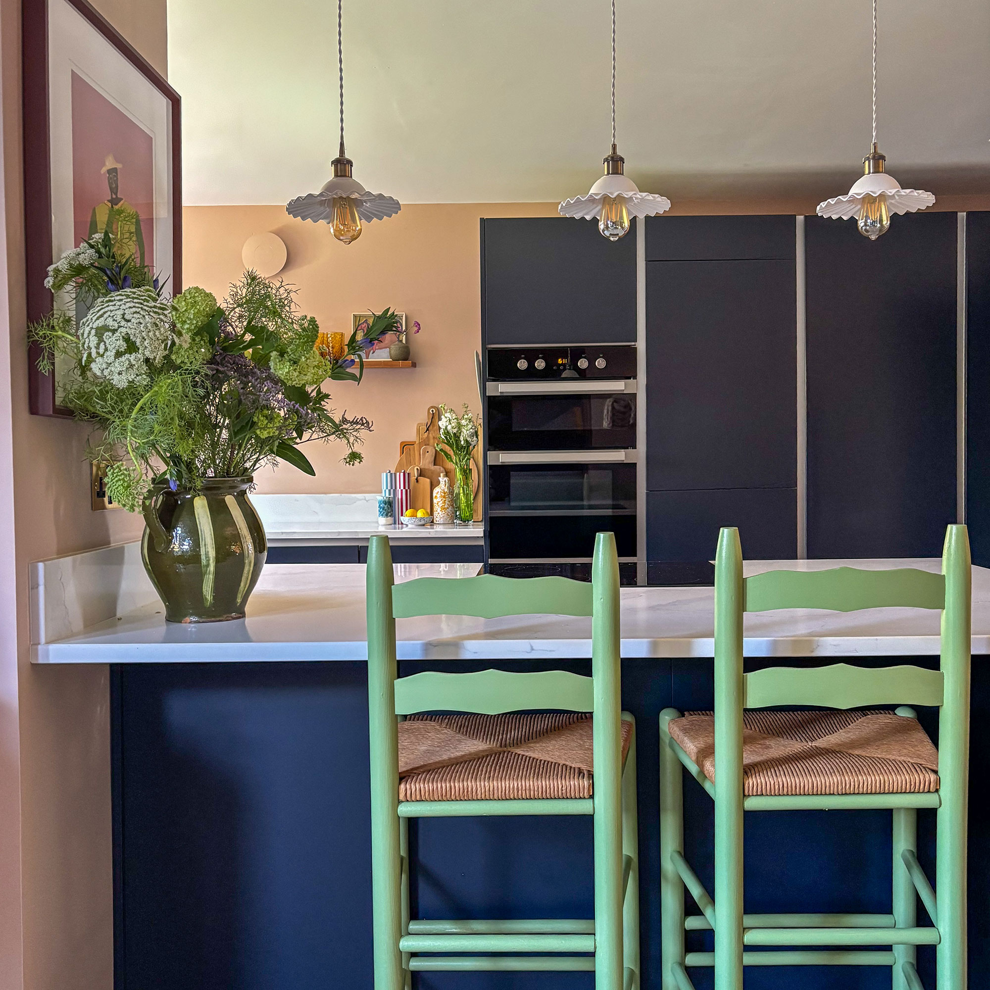 Blue kitchen island with stone top, with two green bar stools, topped with three pendant lights