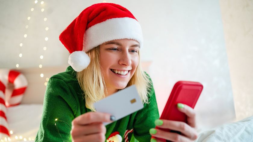 Woman in a Santa hat browses the web on a mobile phone, holding a credit card in her other hand