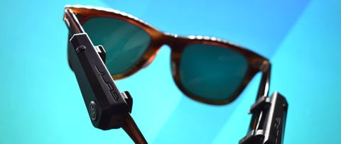 JLab JBuds Frames photograph showing devices on a pair of Ray-Ban sunglasses in front of a blue and teal background